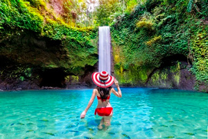 Eine Frau mit Sonnenhut steht im Wasser vor dem Wasserfall.l